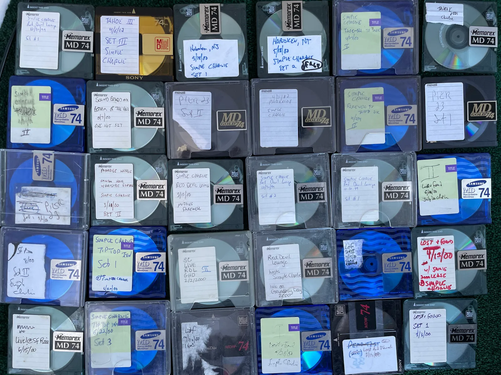 A grid of roughly thirty hand-labeled MiniDiscs of Simple Charlie live recordings, marked with venues and dates around 1999–2002